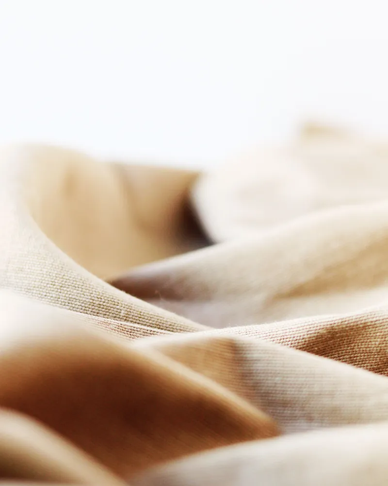 Plis d’un lin beige et brun sous une lumière douce.